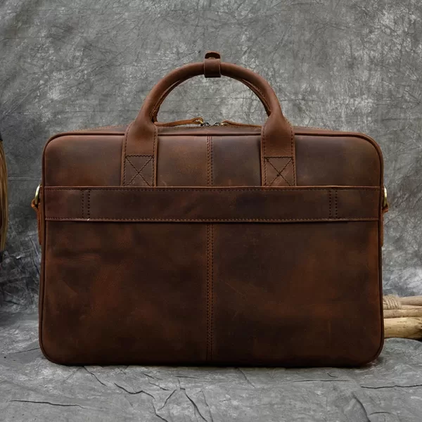 A brown leather briefcase with a handle and two buckles, sitting on a gray table.