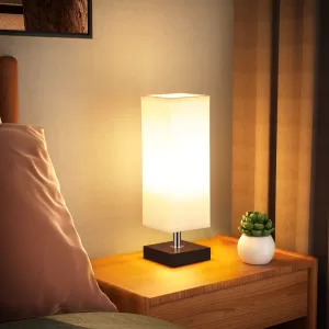 White bedside table lamp with a square flaxen fabric shade, sitting on a wooden nightstand.