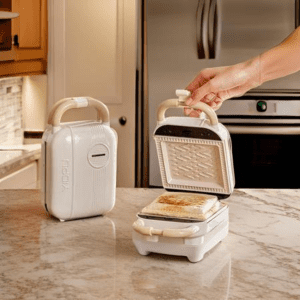 Compact black sandwich maker with golden-brown sandwiches, displayed in a modern Pakistani kitchen.