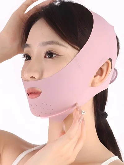 Pink face lifting strap and double chin reducer band worn by a woman, featuring ear cutouts, a mouth opening, small ventilation chin holes, and an adjustable head strap design.