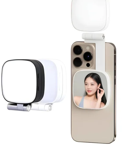 White and black portable LED selfie light featuring a square rounded design with a foldable hinge mount, built-in mini mirror displaying a reflection, attached to the back of a smartphone.