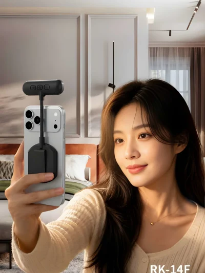 A woman holding a smartphone equipped with a black RK-14F magnetic fill light attached to the back and extending above the camera module.