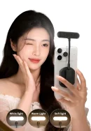 A woman posing next to a smartphone with a black RK-14F magnetic fill light attached to the back, alongside three circular icons illustrating White light, Warm Light, and Soft light modes.
