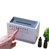 White noise machine with adjustable settings and essential oil diffusers. Hand adjusting settings on a sleep sound machine with aroma diffuser. Relaxation device with sound therapy and aromatherapy. Sleep aid machine with multiple sound options and essential oil bottles.