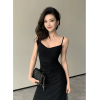 Portrait of a beautiful woman with dark wavy hair wearing a black spaghetti strap dress and holding a quilted chain purse.