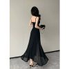 Back view of a woman in a black spaghetti strap maxi dress with a high slit and sheer flowing fabric, holding a small purse.