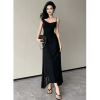 Front view of a stylish woman in a black spaghetti strap maxi dress with a side slit, holding a quilted chain bag and wearing heeled sandals.