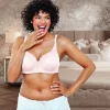 Smiling woman in a light pink bra standing in a bedroom.