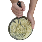 Potato masher mashing cooked potatoes in a glass bowl. Hands using a stainless steel potato masher. Close-up of mashing potatoes with a kitchen utensil. Preparing mashed potatoes with a hand masher.