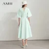 Model wearing AMII backless summer office dress in light color, standing in office environment (2).